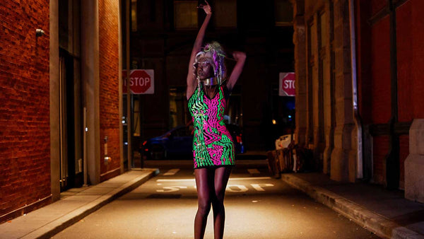 Model wearing neon pink and green Digital Glitch dress standing in a New York City street at night.