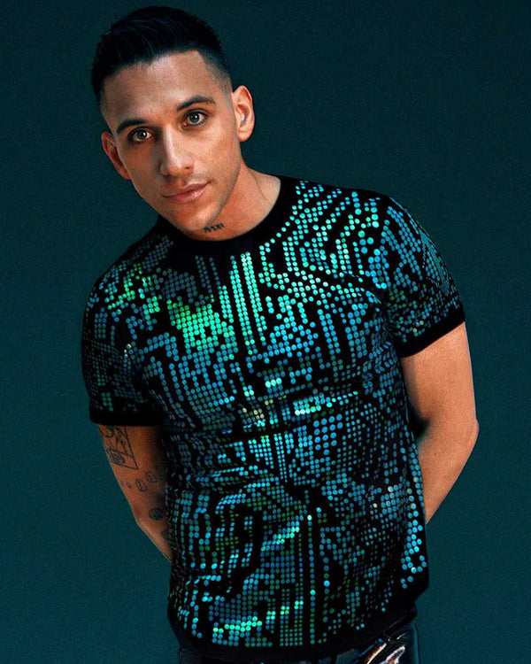 Model wearing electric teal Digital Glitch reflective T-shirt with futuristic pixel-inspired pattern against dark studio background.