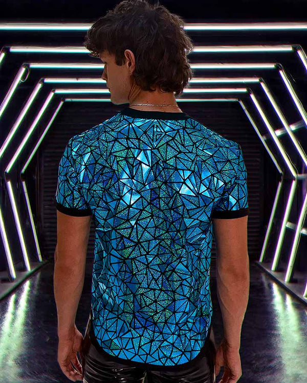 Model wearing blue holographic mosaic tee beneath glowing futuristic tunnel lights with reflective geometric pattern.